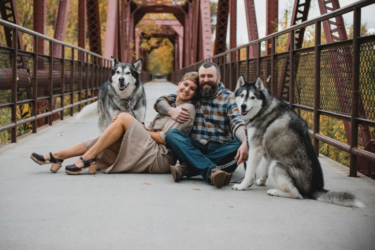 husband and wife with their two huskies on a bridge