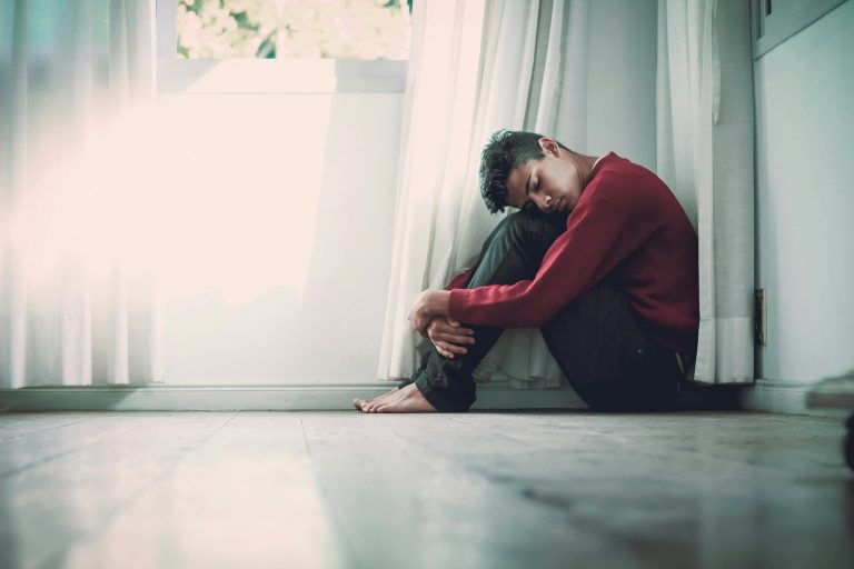 man sitting near window with his knees bent looking anxious